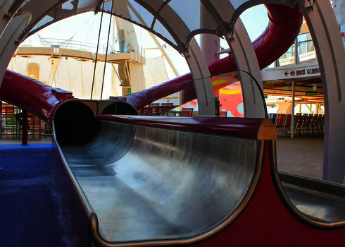 Stainless steel slide exit on a cruise ship with red tube and sun shade.