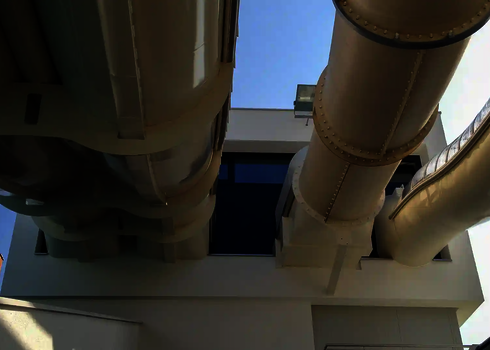 Helle Wasserrutschen mit engen Kurven führen nebeneinander aus weißem Gebäude.