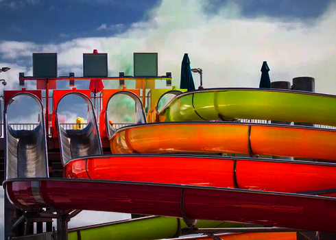 Mehrspurige bunte Wasserrutsche Matracer mit Röhrenstart und offenen Kurven unter blauem Himmel.