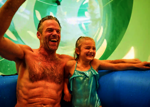 Vater und Tochter rutschen lachend zusammen im Reifen durch die bunte Wasserrutsche RR2700.