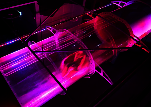 Person rutscht durch einen pink beleuchteten, transparenten Rutschentunnel mit LED-Effekten.