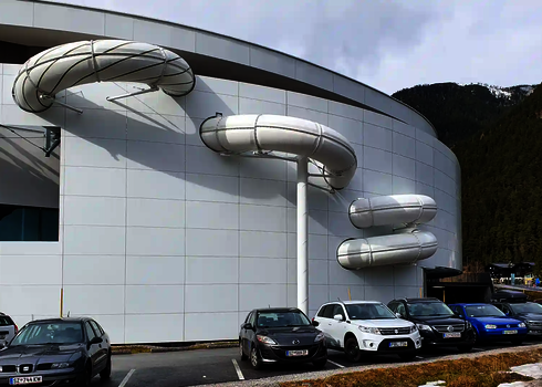 Gedämmte weiße Röhrenrutsche verläuft an der Rückseite eines Schwimmbadgebäudes.