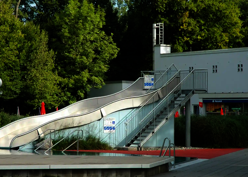 Eine Breitwellenrutsche in einem Schwimmbad, im Hintergrund befinden sich Bäume.