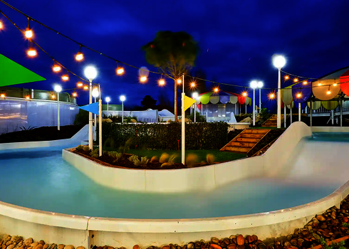 Abendaufnahme des Wildwasserflusses mit Beleuchtung und bunten Sonnensegeln.