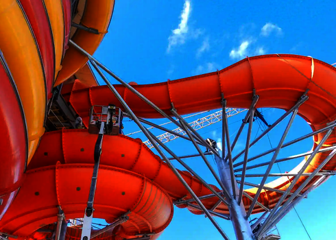 Orangefarbene Family Twister Wasserrutsche mit Stahlkonstruktion unter blauem Himmel.
