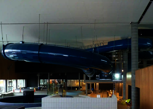 Eine blaue Wasserrutsche hängt an Stahlseilen befestigt von der Decke eines Schwimmbades.