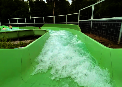 Grüner Wildwasserfluss mit starker Strömung, an den Seiten ein Sicherheitszaun.