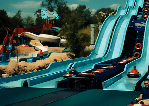 Verschiedene Personen rutschen eine blaue Harakiri Rutsche in einem Wasserpark.