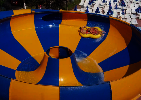 Zwei Menschen in gelbem Rutschreifen rutschen im Raft Bowl, im Hintergrund Liegestühle.