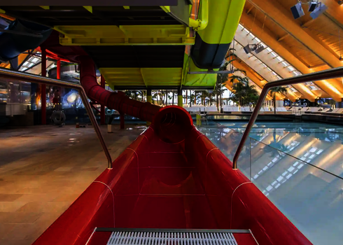 Roter Röhrenrutschenauslauf in einer Indoor-Wasserwelt mit tropischem Ambiente.