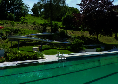 Eine lange WR1040 Rutsche führt durch eine grüne Freibad-Landschaft zum Becken.