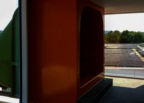 Grüner Rutscheneinstieg in orangefarbener Kabine mit Ausblick, Fassadendurchdringung sichtbar.