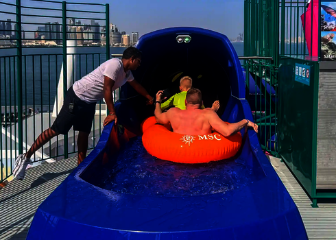 Zwei Personen von hinten, die in einem Rutschreifen im blauen Startbereich einer Wasserrutsche sitzen.