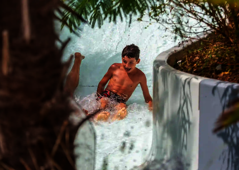 Ein Junge rutscht lachend durch einen Wildwasserfluss.