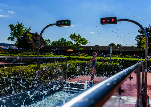 Kind steht im spritzendem Wasser im Freibad, im Auslauf sind Sensorampeln.