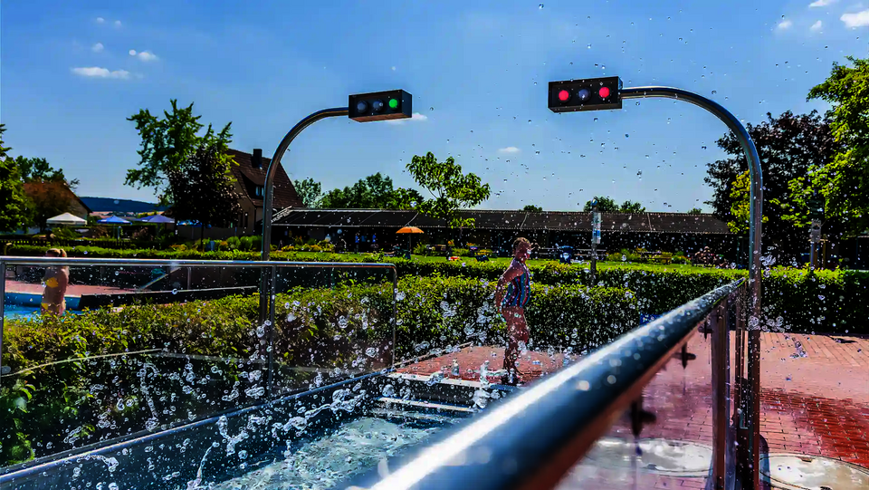 Kind steht im spritzendem Wasser im Freibad, im Auslauf sind Sensorampeln.