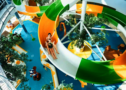 Zwei Personen rutschen eine bunte WR1040 Wasserrutsche in einem Schwimmbad herunter und winken in die Kamera.