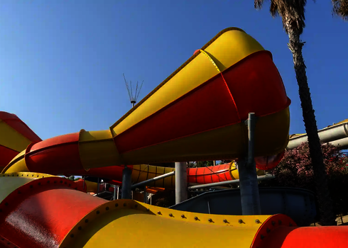 Nahaufnahme eines Crazy Cone in Rot und Gelb mit Stahlstützen vor Palmen.