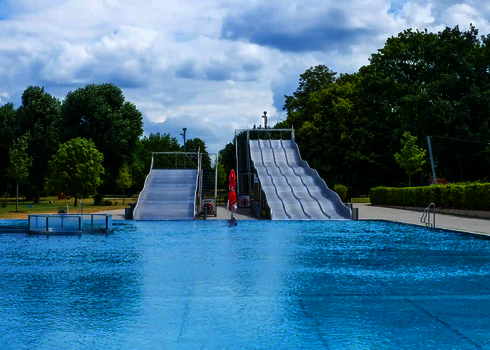 Eine Multilane und eine Breitwellenrutsche im Freibad mit Blick vom Wasserbecken auf die Anlage.