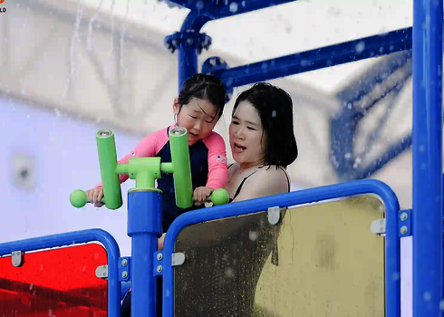 Frau und Kind an einer Wasserspritze auf einer Wasserspielstruktur.