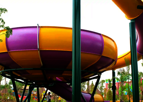 Seitlicher Blick auf ein gelb-violette Raft Bowl Rutsche, getragen von grünen Stahlstützen.