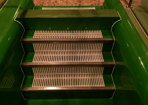 Green slide with steps and handrails, gravel-look floor.