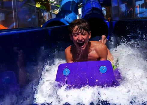 Junge kommt lachend auf einer Rutschmatte im Auslaufbereich einer Wasserrutsche an.