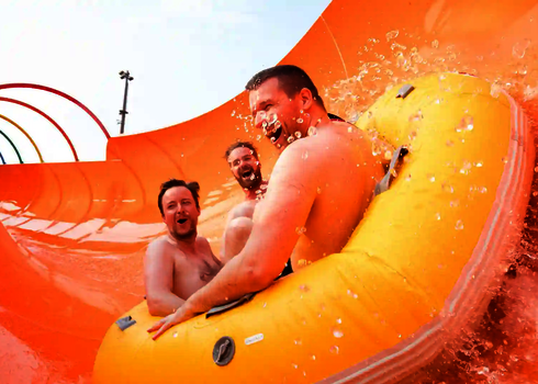 Drei Personen genießen lachend in einem Reifen, die spritzige Fahrt auf einer Wasserrutsche.