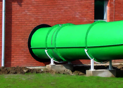 Grüne Wasserrutsche mit gerader Fassadendurchdringung durch rote Backsteinwand.