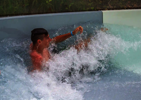 Ein Junge wird im Wasser am Ende des Wildwasserflusses von einer Welle erfasst.