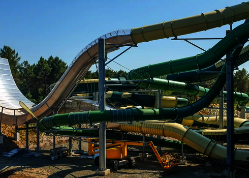 Außenansicht der Boomerang-Rutsche im Aufbau, mit grünen Röhrenrutschen und Baugeräten.