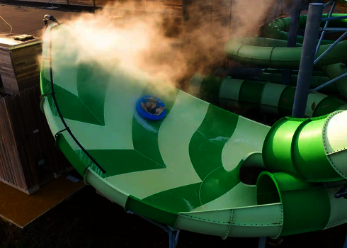 Person fährt auf blauem Rutschreifen durch die nebelige Lotus Wasserrutsche.