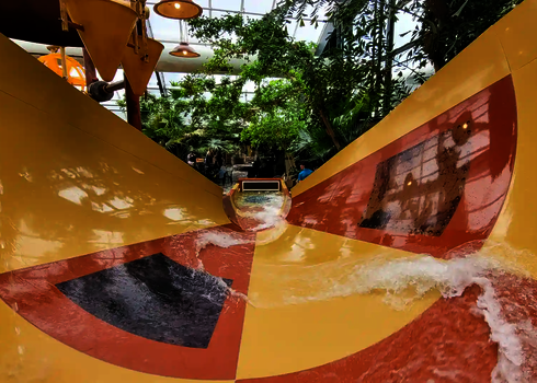 Glänzende GFK Wasserrutsche mit Wasserfluss und Bäumen im Hintergrund.