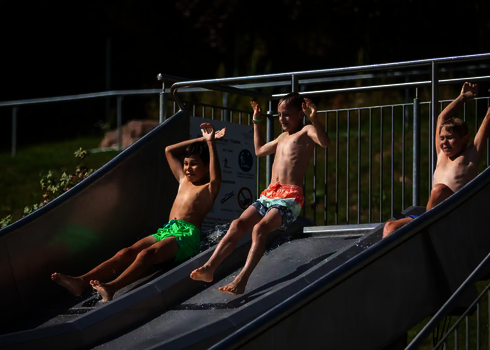 Kinder rutschen nebeneinander auf der Trio-Slide, alle sichtlich begeistert.