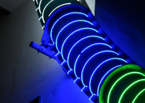 Außenansicht einer Spiralrutsche mit umlaufenden LED-Lichteffekten bei Nacht.