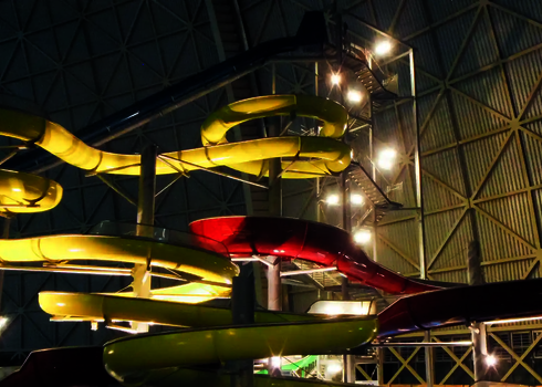 Lange gelbe Wasserrutsche und roter Crazy River in einer überdachten Halle.