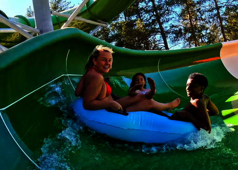Drei Personen rutschen auf einem blauen Mehrpersonenreifen durch den offenen Family Twister.