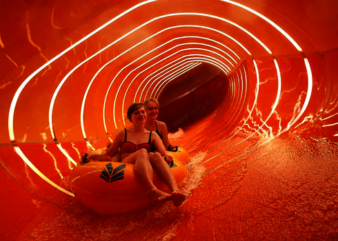 Zwei Personen rutschen auf gelbem Reifen durch eine orangene Family Twister Wasserrutsche.