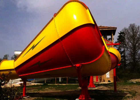 Rote Body Cone Wasserrutsche auf Stahlstützen vor Bäumen und Rutschenturm.