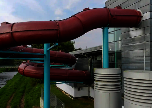 Eine rote RR1200 Wasserrutsche außen an einem Hallenbad verlaufend.