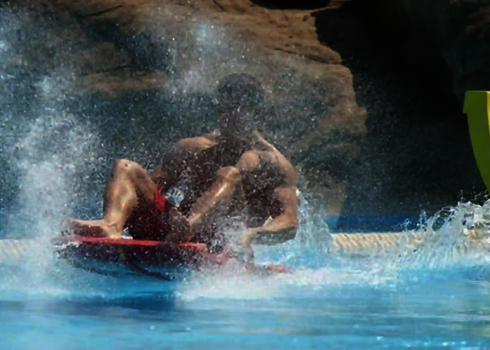 Mann sitzt im spritzendem Wasser Auf dem Aqua Shuttle Brett.