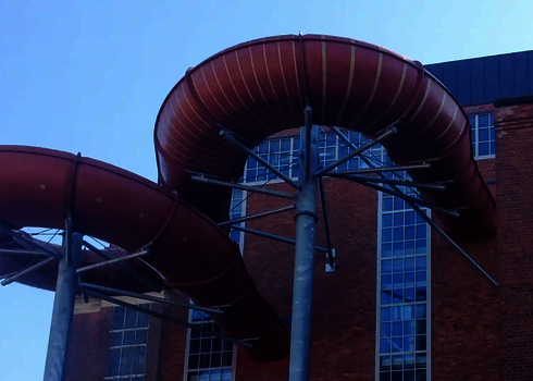 Rote Family Twister Wasserrutsche mit Kurven vor einem Backsteingebäude.