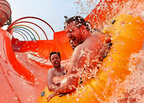 Nahaufnahme von spritzendem Wasser und Personen, die lachend in einem Rutschreifen sitzen.