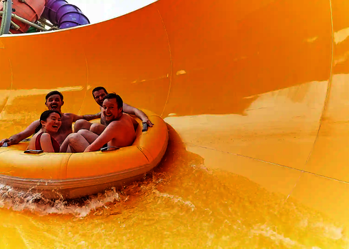 Vier Personen rutschen lachend durch den gelben Trichter der RR2700 mit bunten Röhren im Hintergrund.