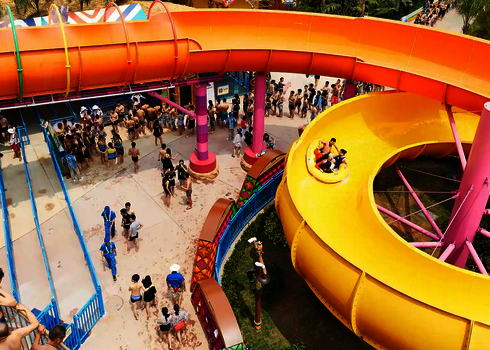 Wasserpark mit vielen Menschen, rechts eine gelbe kreisförmige Wasserrutsche.