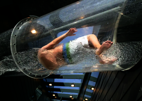 Eine Person rutscht durch eine durchsichtige Acryl-Wasserrutsche mit Wasserverwirbelung.