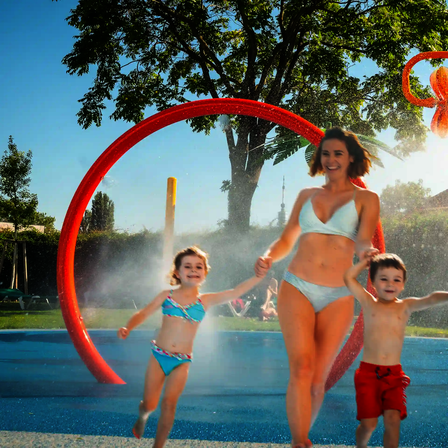 Frau hält lachend zwei Kinder an der Hand, im Hintergrund Wie-Spray Element "Spühring".