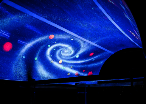 Spiralförmige Galaxie mit bunten Planeten auf der Innenfläche eines Rutschenteils unter UV-Licht.