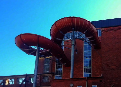 Eine rote Wasserrutsche führt in einer Kurve durch die Backsteinfassade eines Gebäudes.