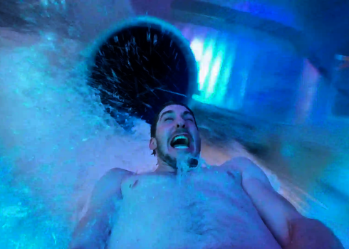 Nahaufnahme eines Mannes der in einer blau leuchtenden Wasserrutsche rutscht.